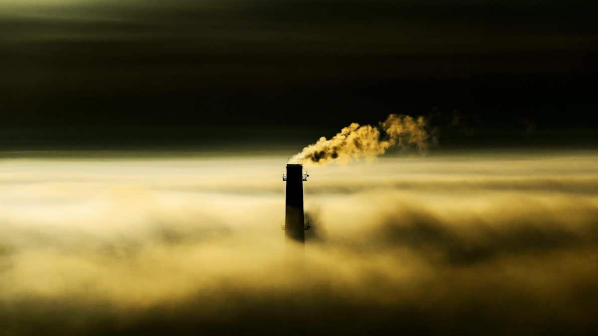 Chimney emitting smoke through dense fog, highlighting air pollution concerns.