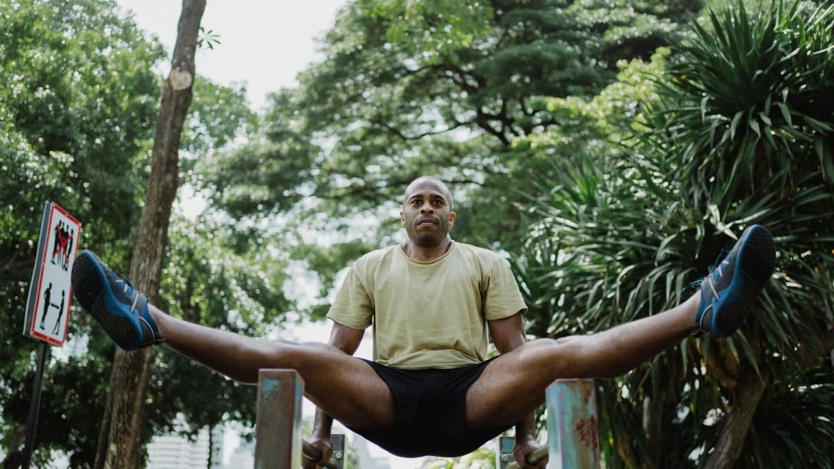 Man performing gymnastics on parallel bars in a park. Fitness and strength training outdoors.