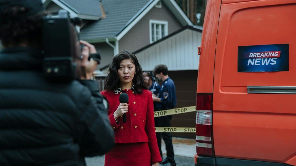 Female reporter in red with microphone reporting live at an outdoor crime scene with a news van.