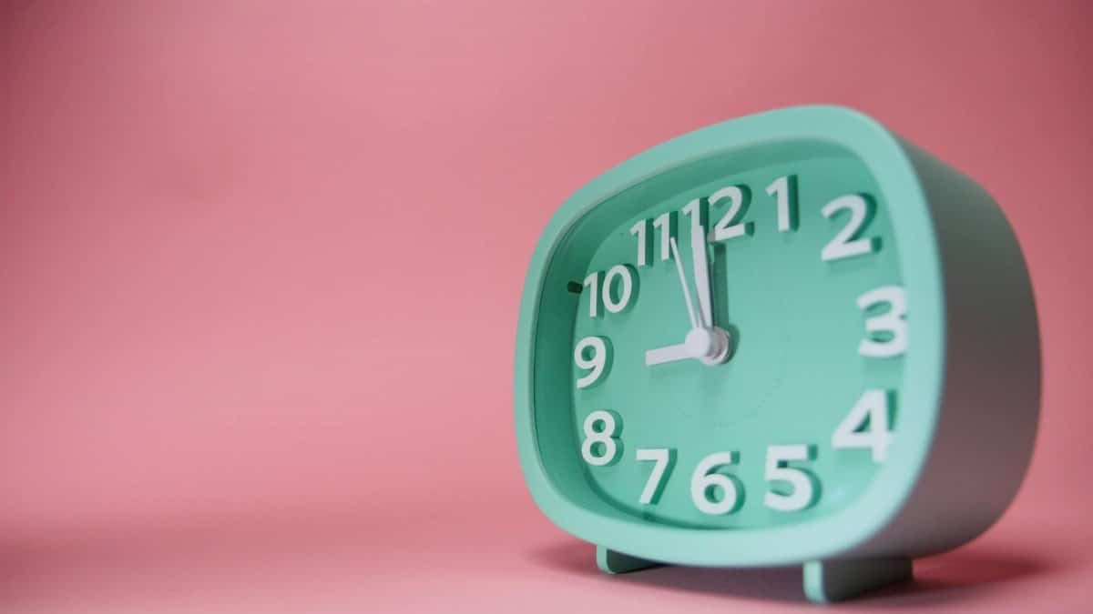 A mint green alarm clock displayed against a pastel pink background. Concept of time.