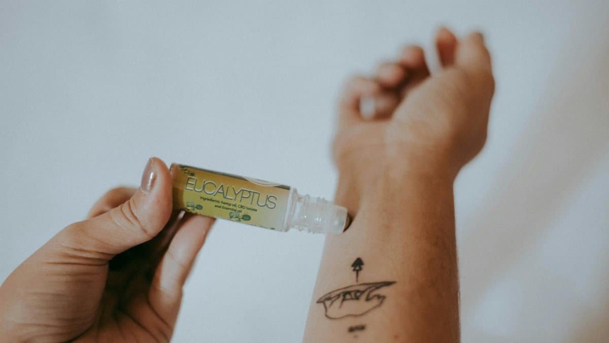 Close-up of eucalyptus essential oil being applied to a tattooed arm for relaxation.