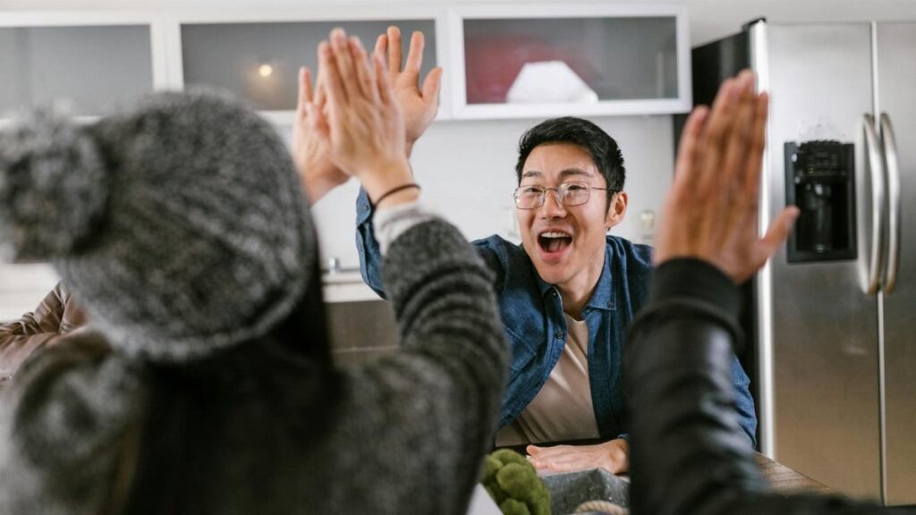 A diverse group of adults sharing a celebratory high five in a modern kitchen setting.
