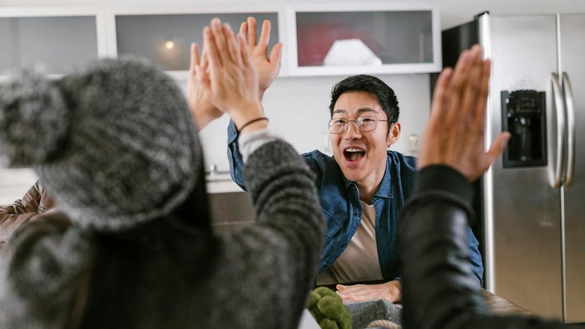 A diverse group of adults sharing a celebratory high five in a modern kitchen setting.