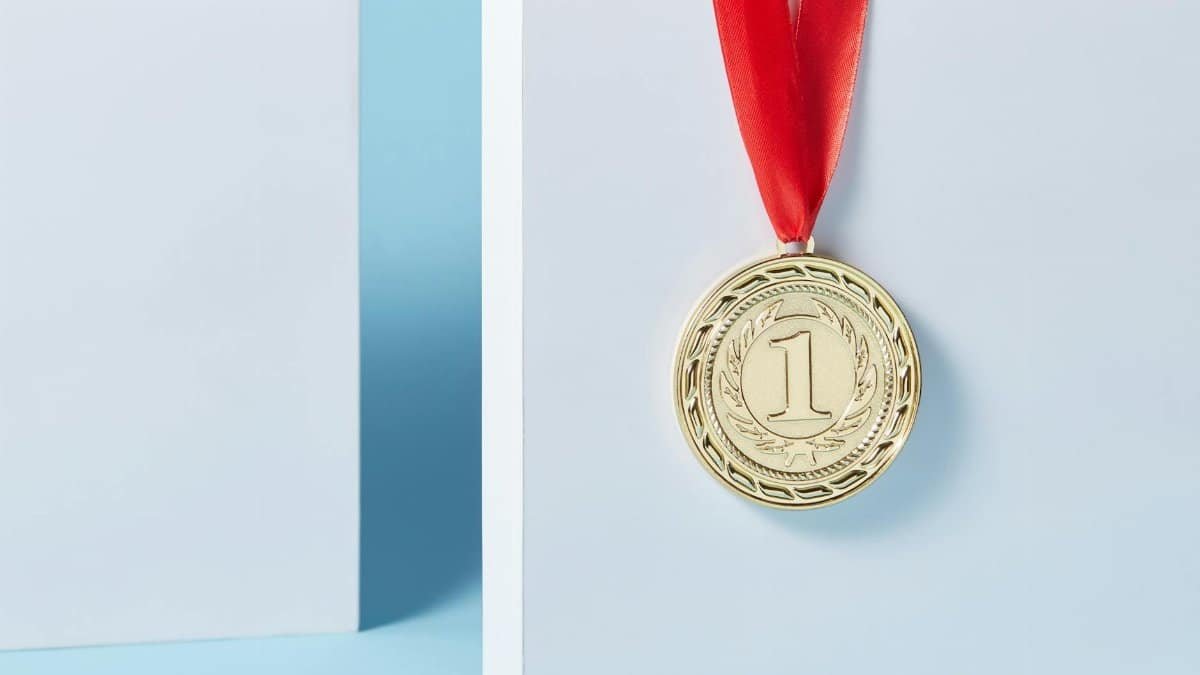 Close-up of a gold medal with a red ribbon hanging against a light blue background.