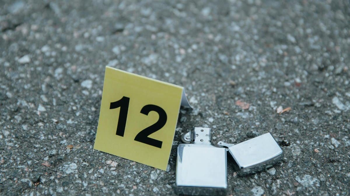 A detailed close-up of a lighter at a crime scene marked with an evidence number sign on concrete.