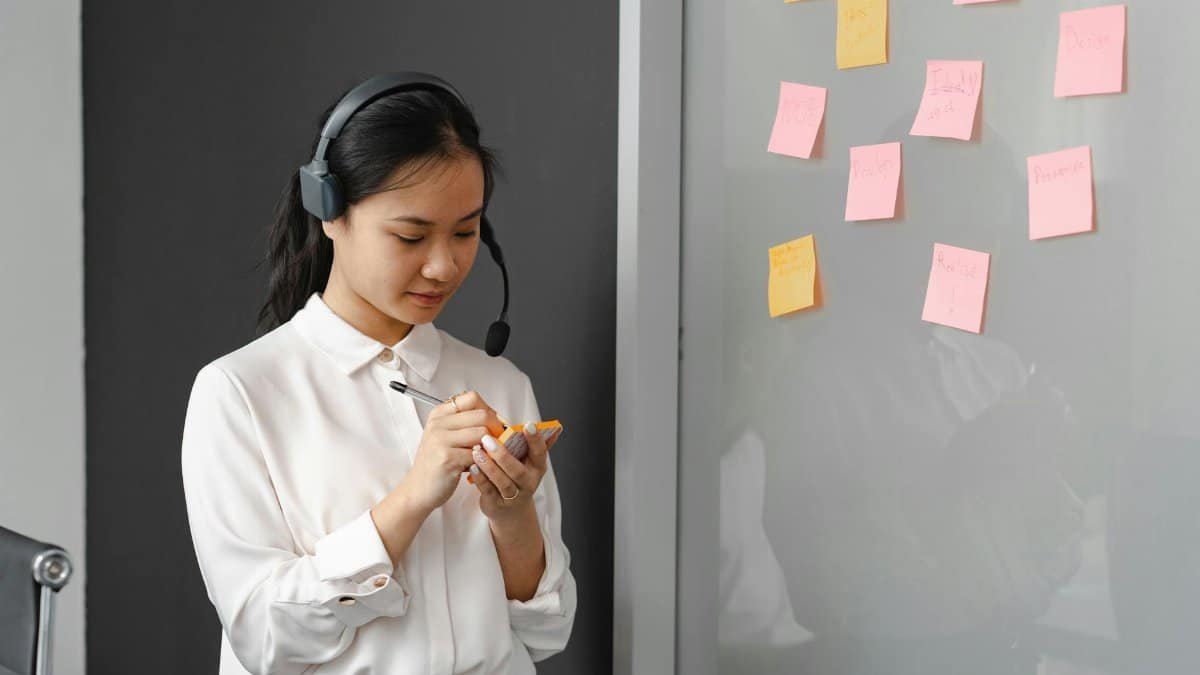 A woman in a call center writing on sticky notes with a headset indoors.