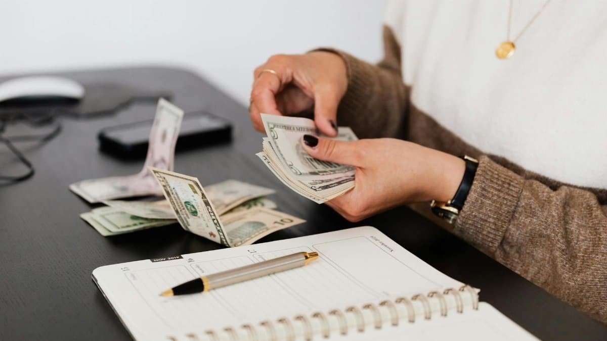Close-up of person counting cash with notepad on desk, indicating financial tasks.