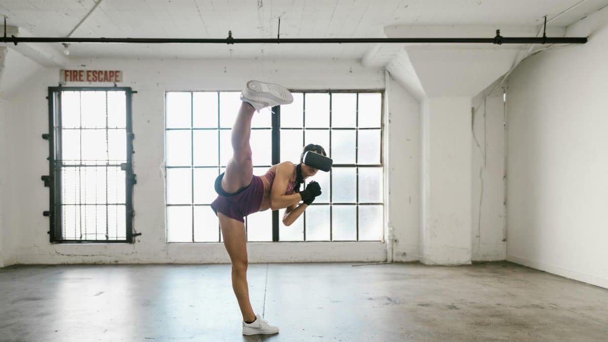 Woman using VR headset for fitness training. Full shot in an industrial-style studio.