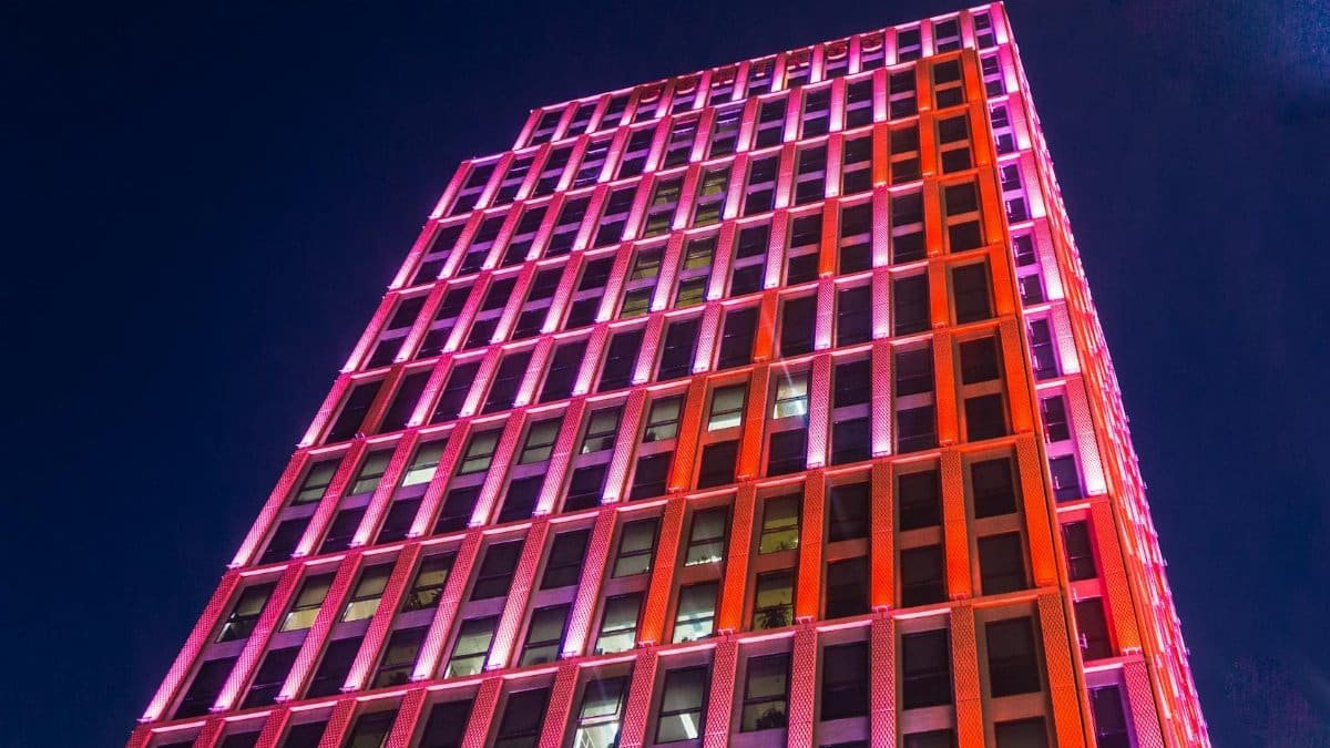 Vibrant pink and orange lights illuminate a skyscraper against a night sky.