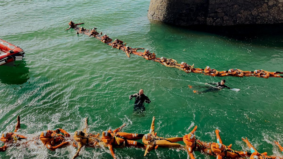 People participating in a water rescue training exercise, linked by life vests.