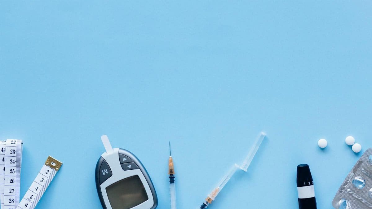Flat lay of diabetes management tools including glucose meter, syringe, and pills on blue background.