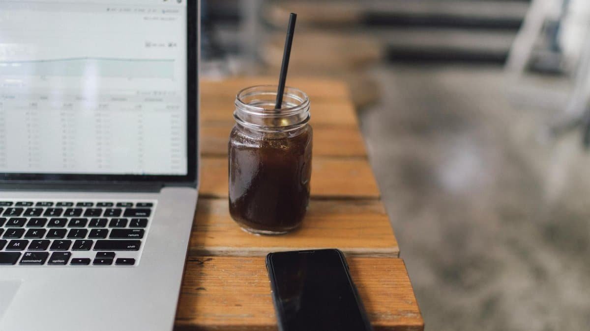 A cozy workspace featuring a laptop, coffee in a mason jar, and a smartphone on a wooden table.