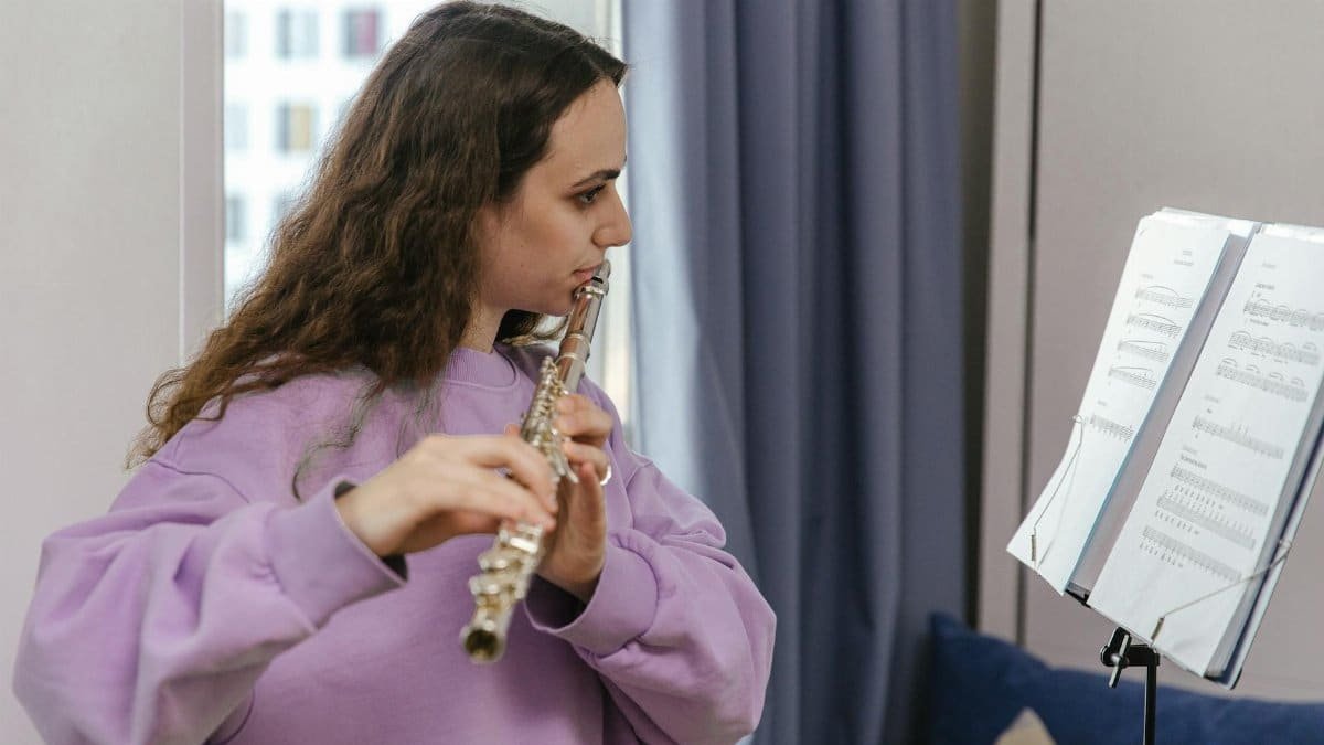Side view of a woman playing the flute, reading sheet music, indoors.