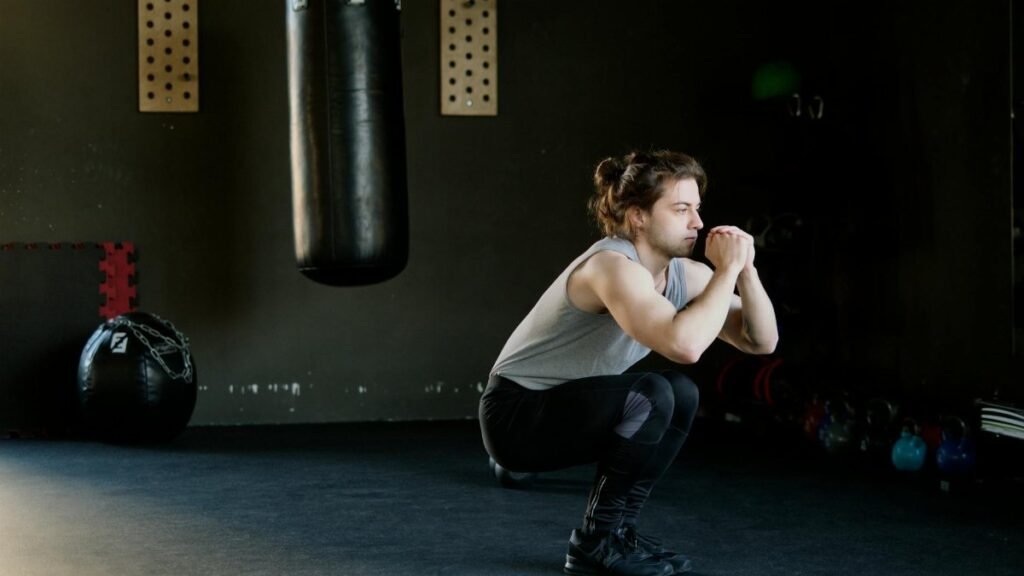 A man is doing squats in a gym with a punching bag. The setting appears stylish and focused on fitness.