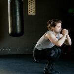 A man is doing squats in a gym with a punching bag. The setting appears stylish and focused on fitness.