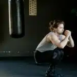 A man is doing squats in a gym with a punching bag. The setting appears stylish and focused on fitness.