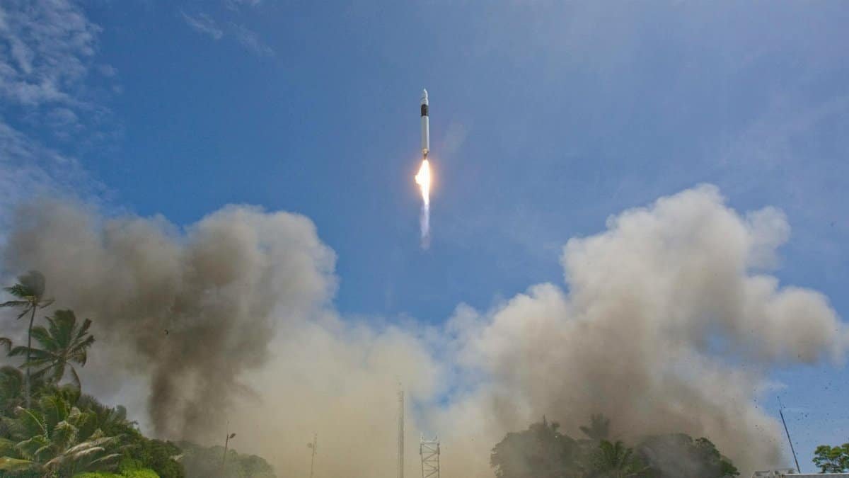 A rocket launches into a clear blue sky, leaving smoke and flames behind.