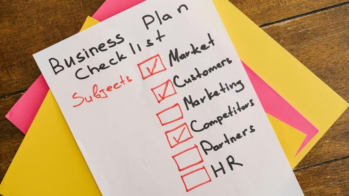 A handwritten business plan checklist on a table with colorful papers indicating important topics for startups.