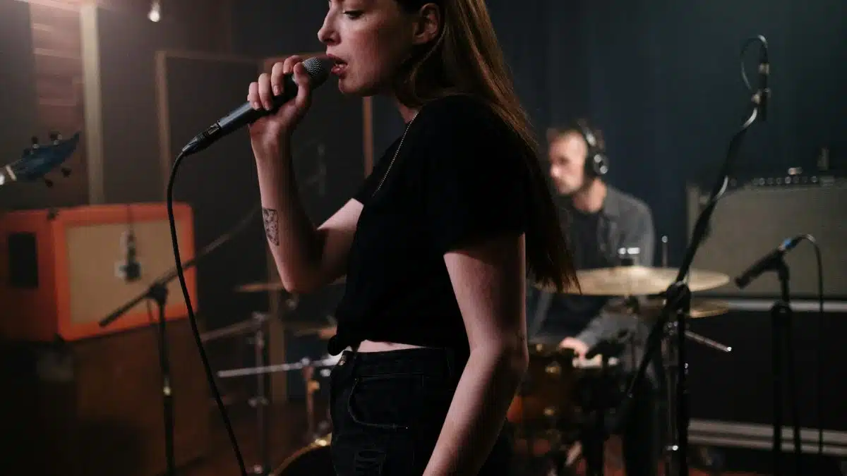 A female singer passionately performs during a band practice session in a music studio.