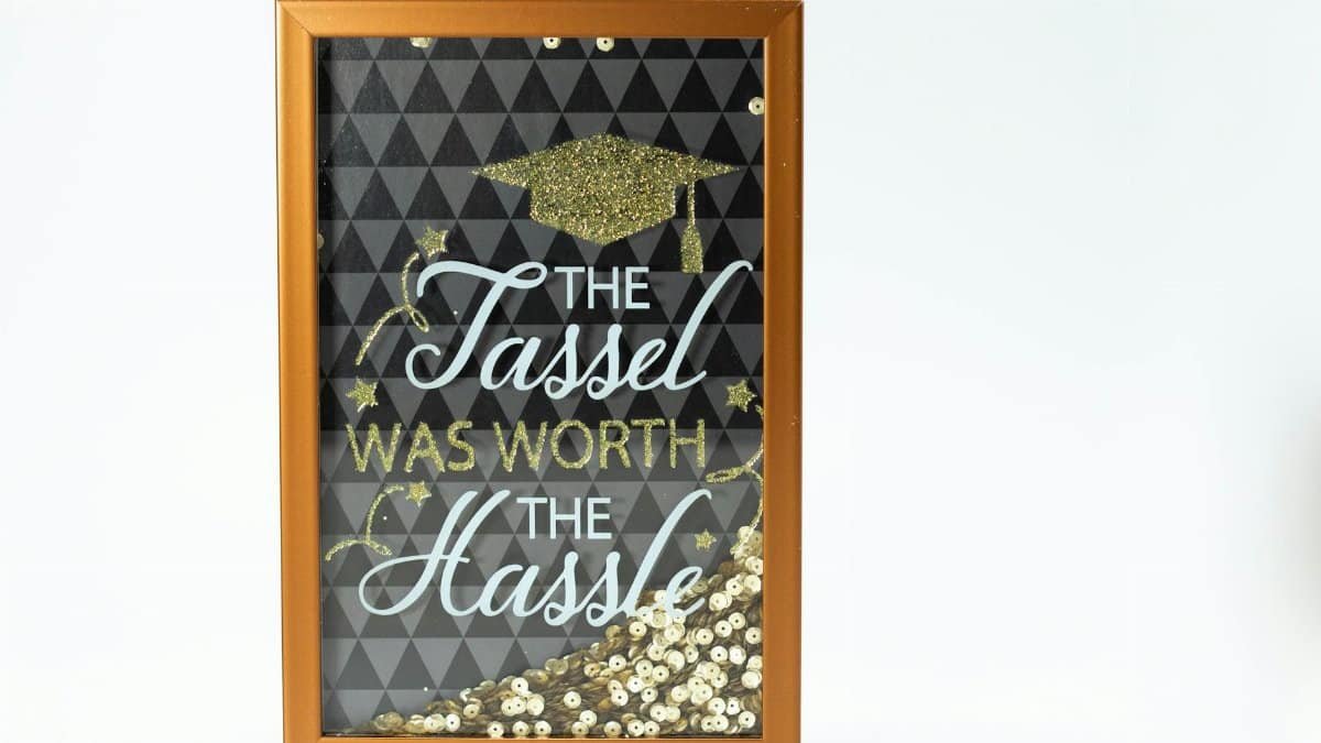 Framed graduation quote "The Tassel Was Worth the Hassle" adorned with glitter on a white background.
