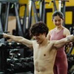 Man and woman exercising with dumbbells in a gym setting, focused on strength training.