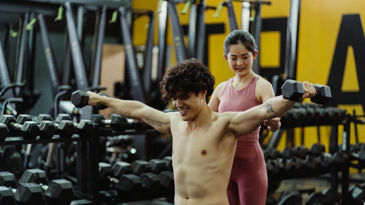Man and woman exercising with dumbbells in a gym setting, focused on strength training.