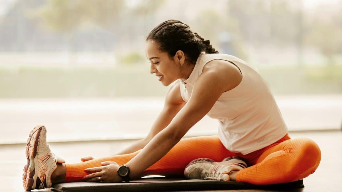 A woman performing a hamstring stretch indoors, promoting fitness and flexibility.