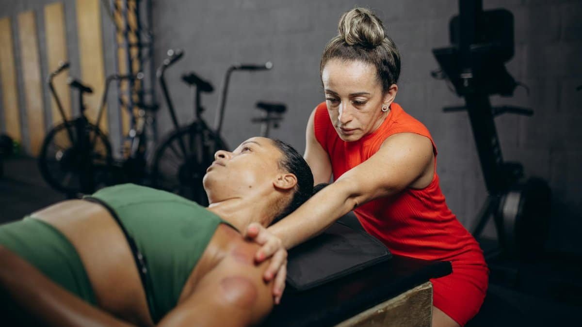 A therapist assists a woman with manual therapy to improve flexibility and mobility in a gym environment.