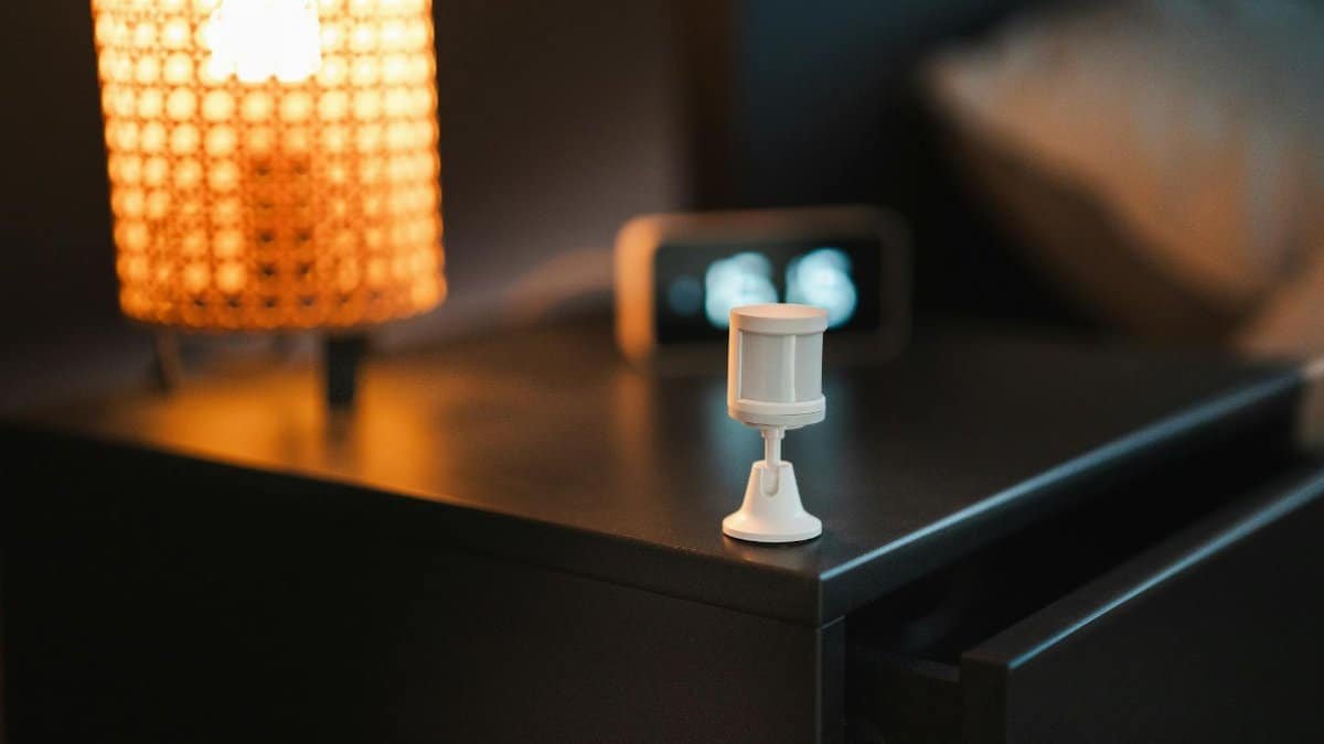 Stylish bedroom with smart motion sensor, lamp, and alarm clock on wooden nightstand.