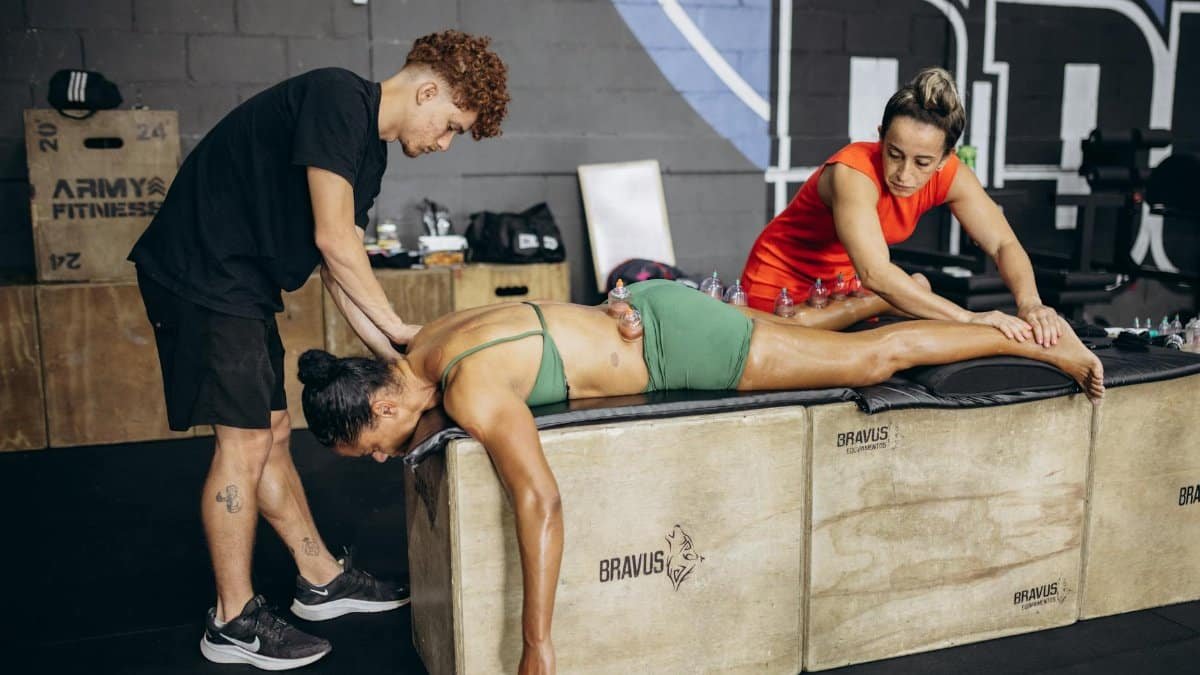 Athlete receives cupping therapy for muscle recovery in a gym setting with two therapists.