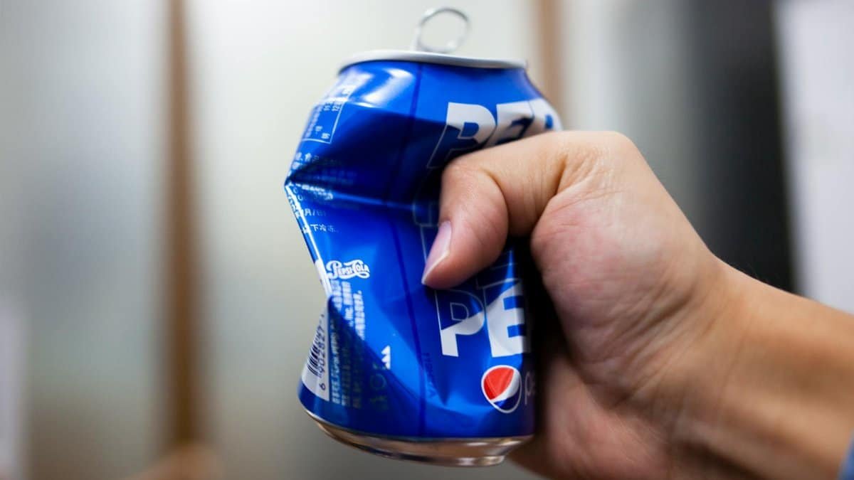 Hand crushing a blue soda can with blurred background, symbolizing strength and recycling.