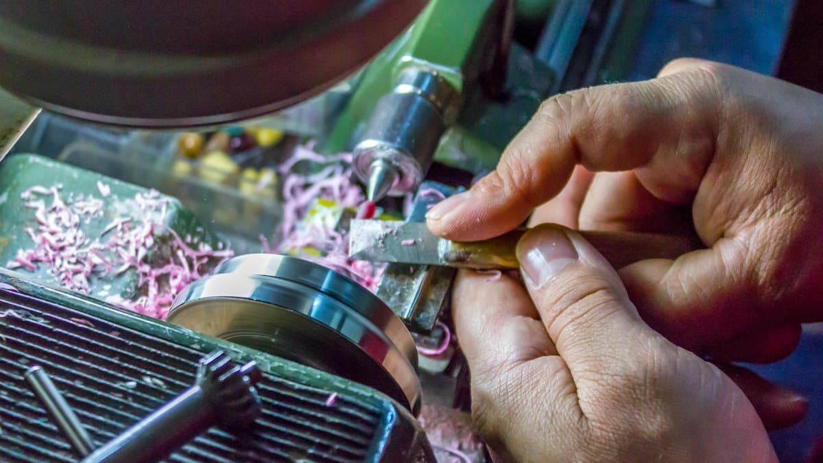 Hands carefully operate a metal lathe machine, showcasing precision in metalworking.