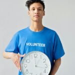 Young male volunteer in blue shirt holding a clock, symbolizing time management.
