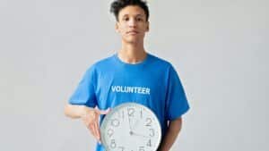Young male volunteer in blue shirt holding a clock, symbolizing time management.