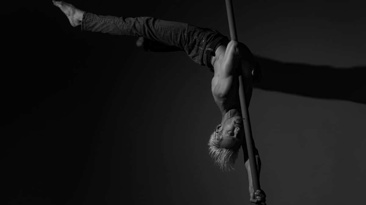 A skilled acrobat performs an impressive pole routine in a dramatic black and white setting.