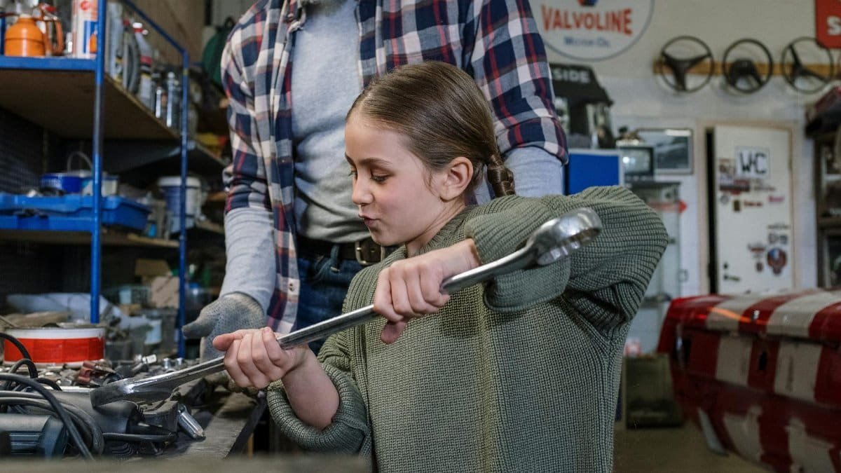 Father and daughter bond while fixing a car in a workshop.