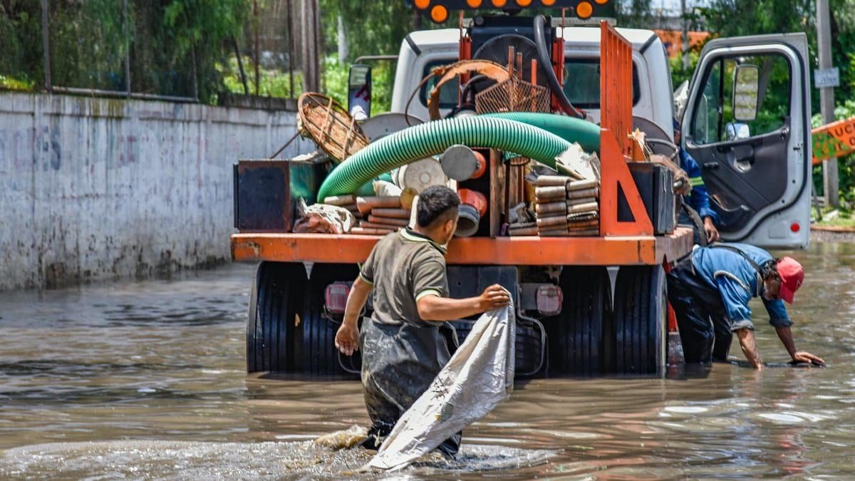 Workers wading through floodwaters near a truck, managing a city crisis after heavy rain.