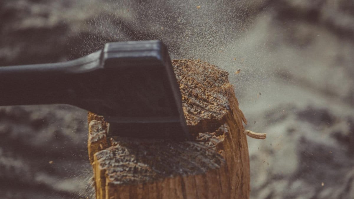 Close-up of an axe striking a wood log outdoors, creating dust and splinters.