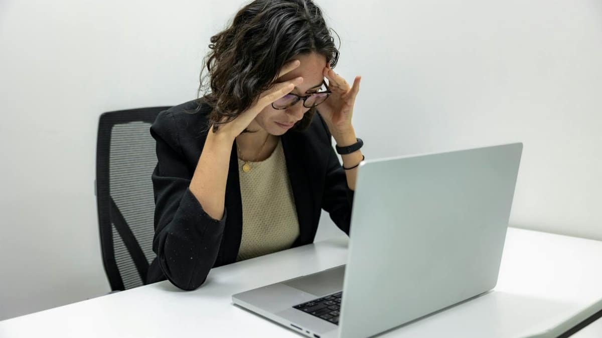 A young woman experiencing stress and fatigue while working on her laptop in an office setting.