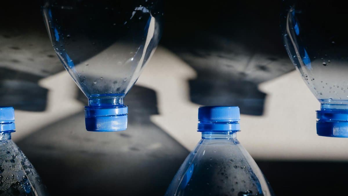 Close-up of plastic bottles with blue caps casting shadows, highlighting recycling themes.