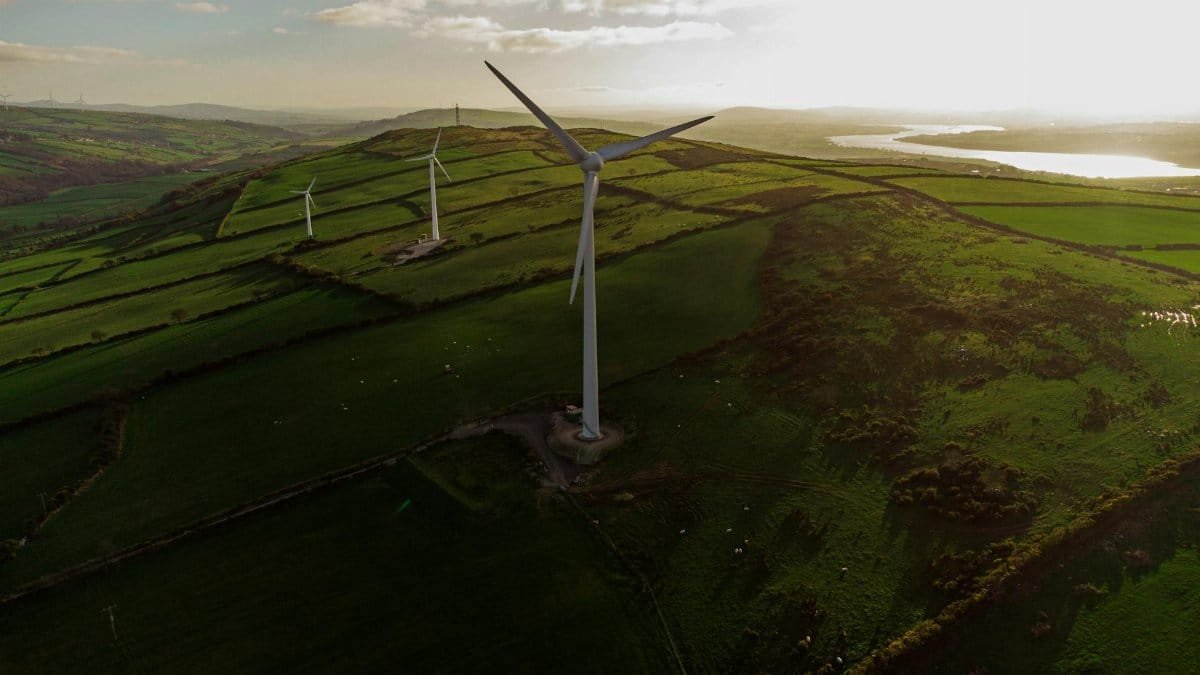 Scenic aerial view of wind turbines in rolling green fields at sunset, promoting renewable energy and sustainability.