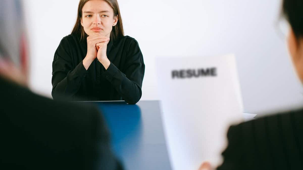 A woman in a job interview facing two employers with a focus on her resume.