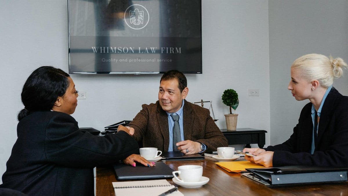 Group of multiracial coworkers in formal suits gathering at table with documents and coffee while shaking hands after verdict in court