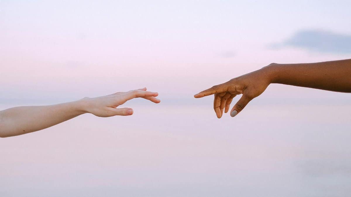Two diverse hands reaching out across a pastel horizon, symbolizing unity and connection.