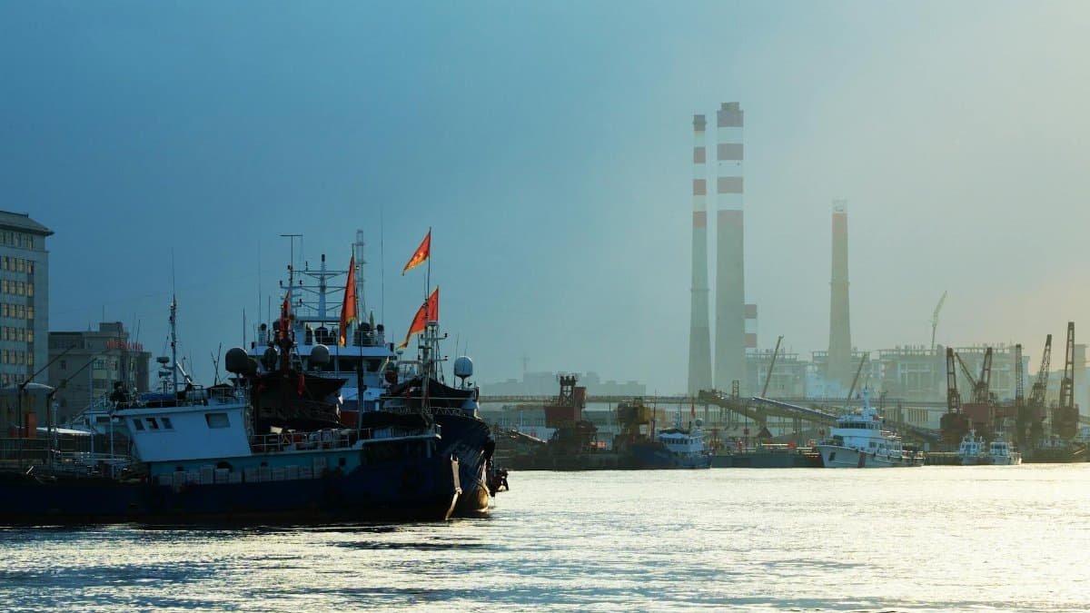 Industrial harbor scene with ships and smokestacks at dusk, creating a serene yet busy atmosphere.