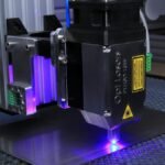 Close-up of a laser engraving machine operating on a metal surface with blue laser light.