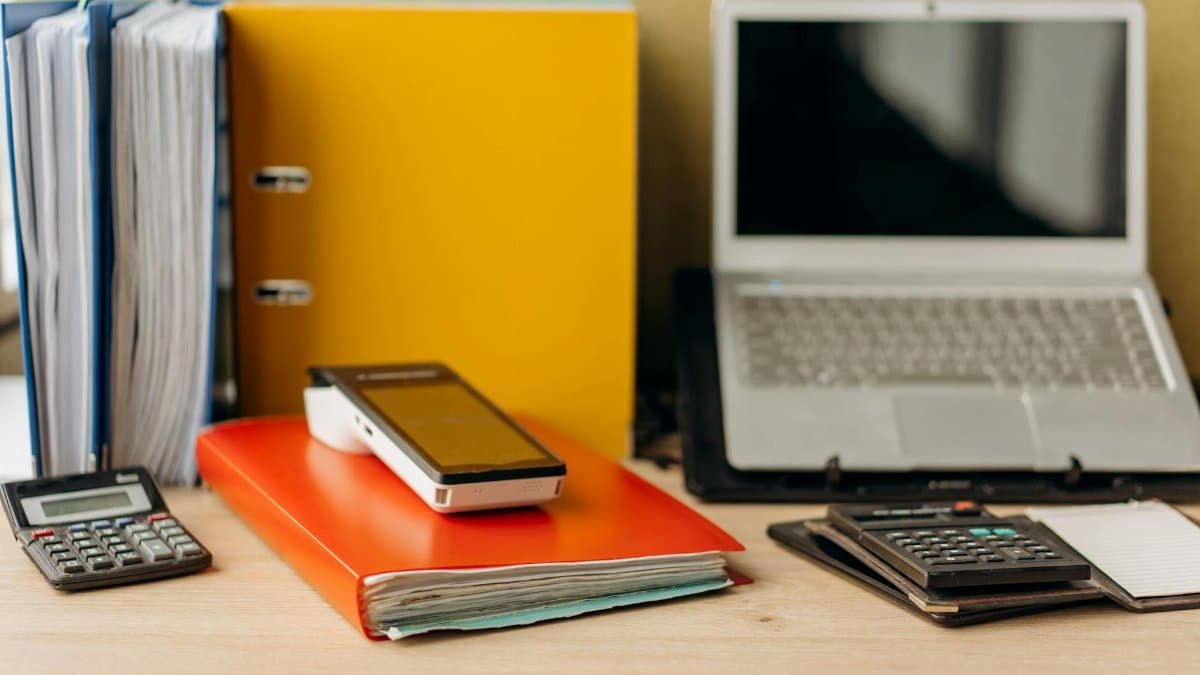 Office desk setup with laptop, documents, and calculators, ideal for business productivity.