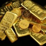 A close-up of gold bars and coins symbolizing wealth and investment on a black background.