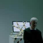 A senior adult sits indoors next to a computer wrapped in caution tape, symbolizing job loss and unemployment.