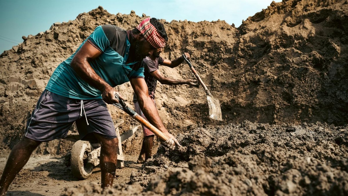 Two workers engaged in intensive digging at a construction site under blue skies.